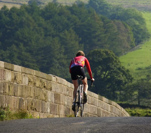 a cyclist in red lycra top descending a hill with trees and hills in the background